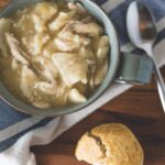 Chicken and Dumplings in a bowl on a counter next to a bread roll
