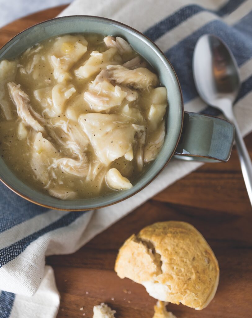 Chicken and Dumplings in a bowl on a counter next to a bread roll