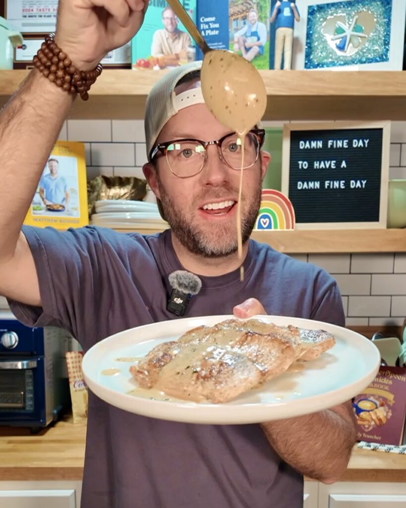 Matthew Bounds holding a plate of Creamy Tarragon Mustard Pork Chops and pouring more sauce on the pork chops