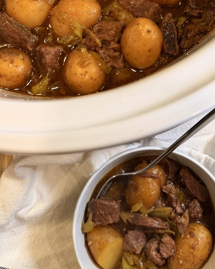 Slow Cooker Italian Beef and Gravy in a bowl on a table next to crockpot with rest of food 
