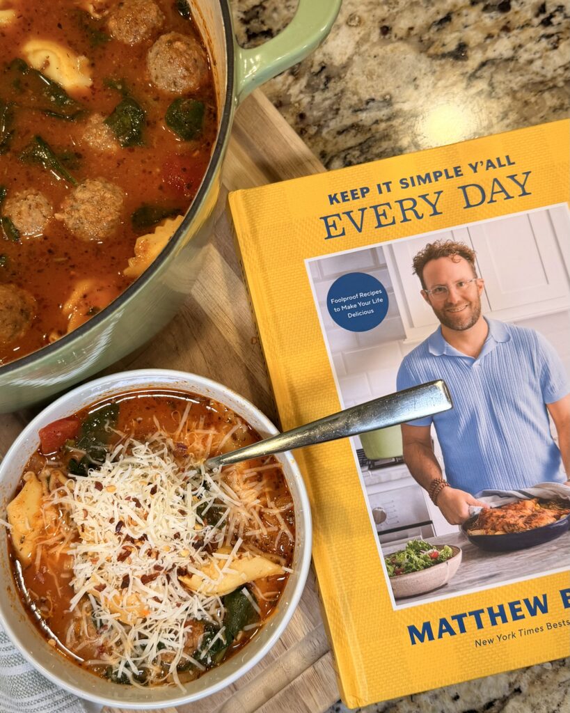 A bowl of Tortellini Soup from Your Barefoot Neighbor Matthew Bounds' book Keep It Simple Y’all Everyday sits on the counter next to the book. 
