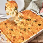 Your Barefoot Neighbor's Broccoli and Cheese Casserole being spooned onto a plate from a baking dish. The casserole is creamy and rich.