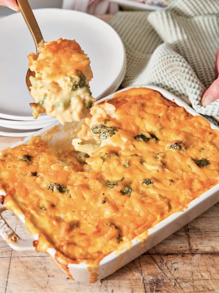 Your Barefoot Neighbor's Broccoli and Cheese Casserole being spooned onto a plate from a baking dish. The casserole is creamy and rich.