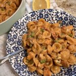 A hearty helping of one pan chicken pea pasta, prepared by Your Barefoot Neighbor Matthew Bounds, is on a plate next to sliced lemons
