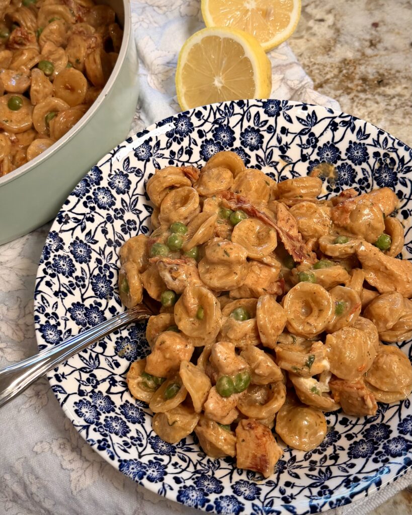 A hearty helping of one pan chicken pea pasta, prepared by Your Barefoot Neighbor Matthew Bounds, is on a plate next to sliced lemons