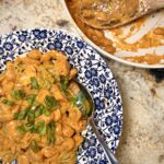 Buffalo chicken broccoli mac n cheese in a bowl next to a skillet full of the dish.
