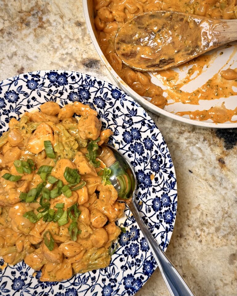 Buffalo chicken broccoli mac n cheese in a bowl next to a skillet full of the dish.