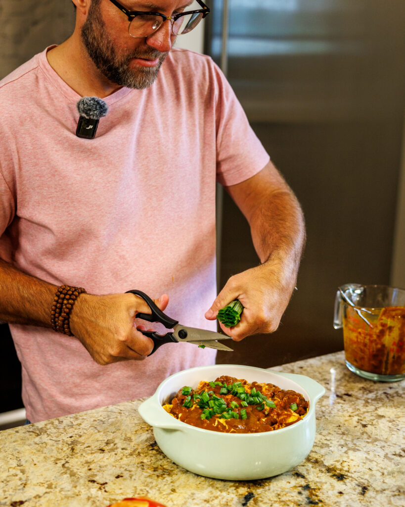 Matthew Bounds, creator of Your Barefoot Neighbor, cuts green onions to put on top of a hearty bowl of Chili Frito Pie
