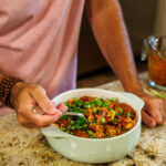 A hearty bowl of Your Barefoot Neighbor's Chili Frito Pie sits on the kitchen counter, while Matthew Bounds digs into the pie with a spoon