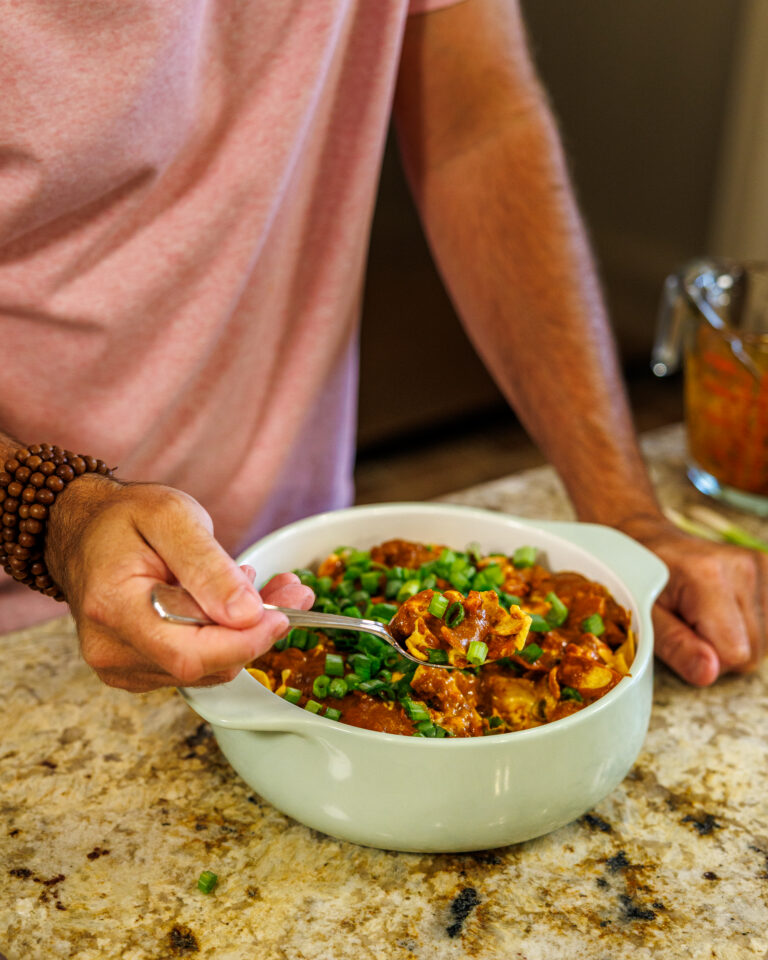 A hearty bowl of Your Barefoot Neighbor's Chili Frito Pie sits on the kitchen counter, while Matthew Bounds digs into the pie with a spoon