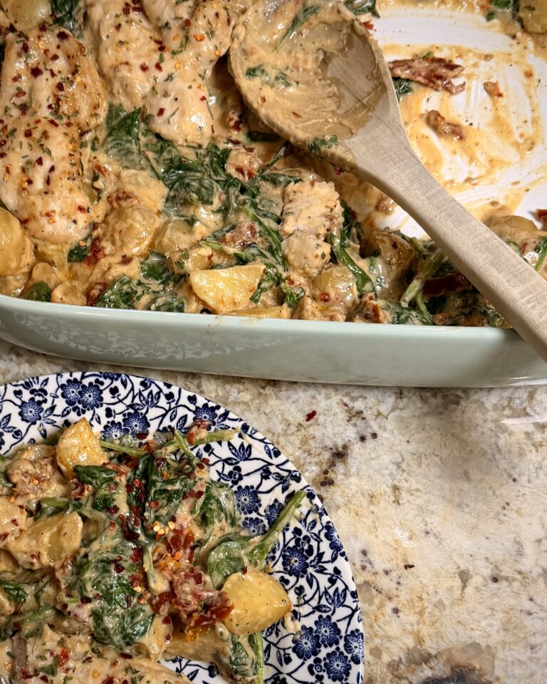 Creamy Spinach Alfredo Potatoes and Chicken sits on a counter next to a plate with a sizable helping.