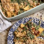 Creamy Spinach Alfredo Potatoes and Chicken sits on a counter next to a plate with a sizable helping.