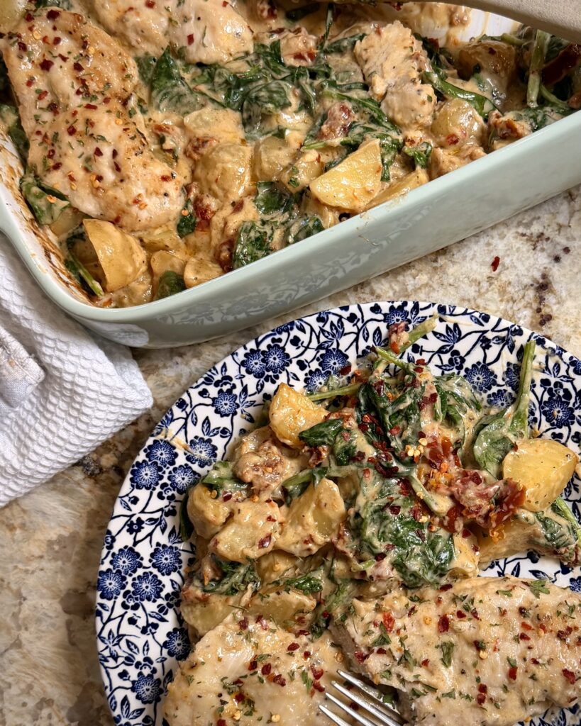Creamy Spinach Alfredo Potatoes and Chicken sits on a counter next to a plate with a sizable helping.