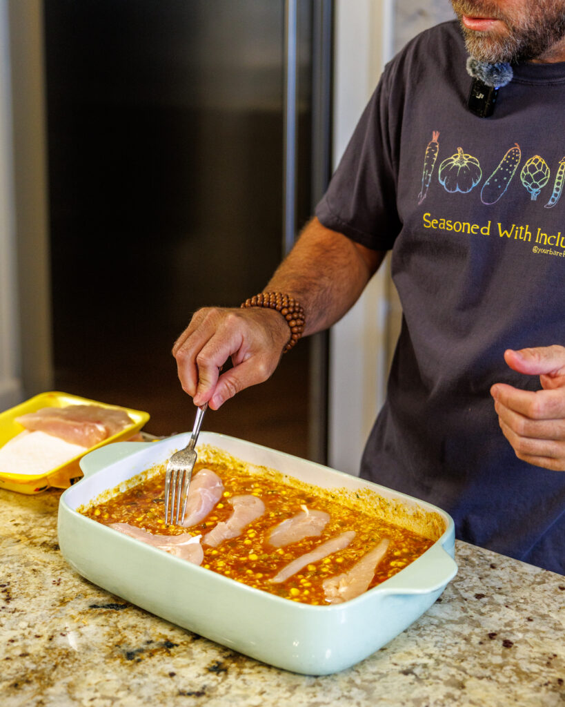 Your Barefoot Neighbor Matthew Bounds adds ingredients to his dish for his Baked Swim Queso Chicken in his kitchen