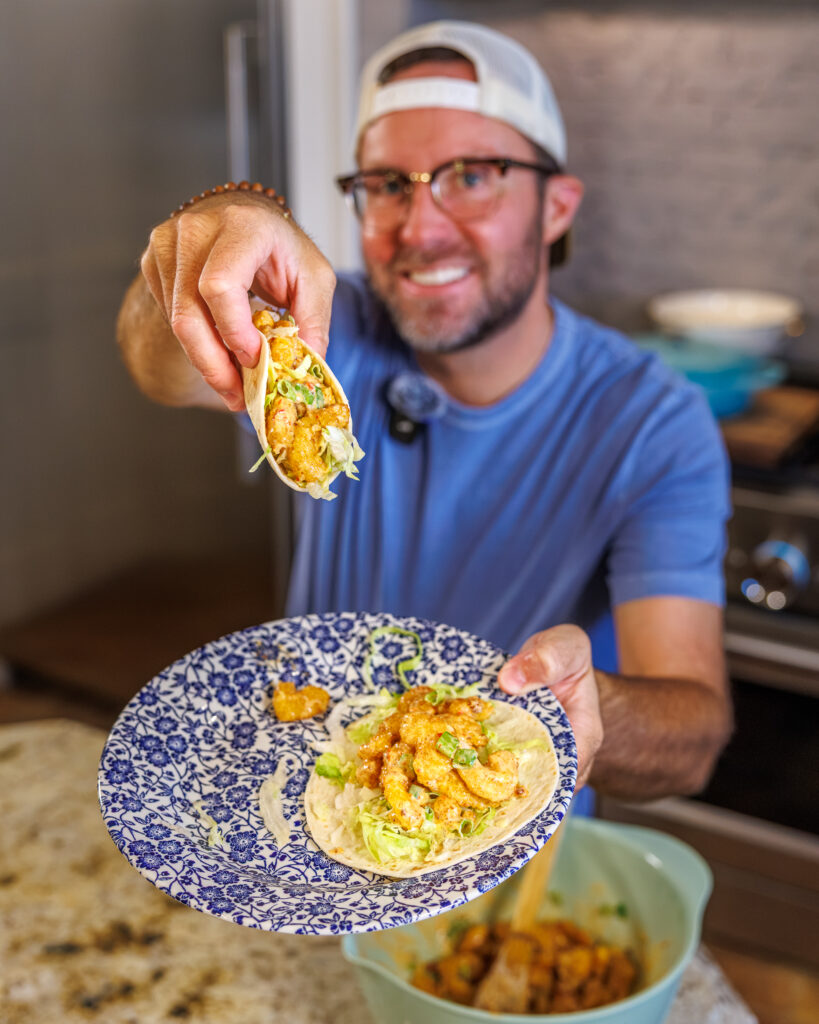 Matthew Bounds, creator of Your Barefoot Neighbor, holds a plate of his Bang Bang Shrimp Tacos in his kitchen