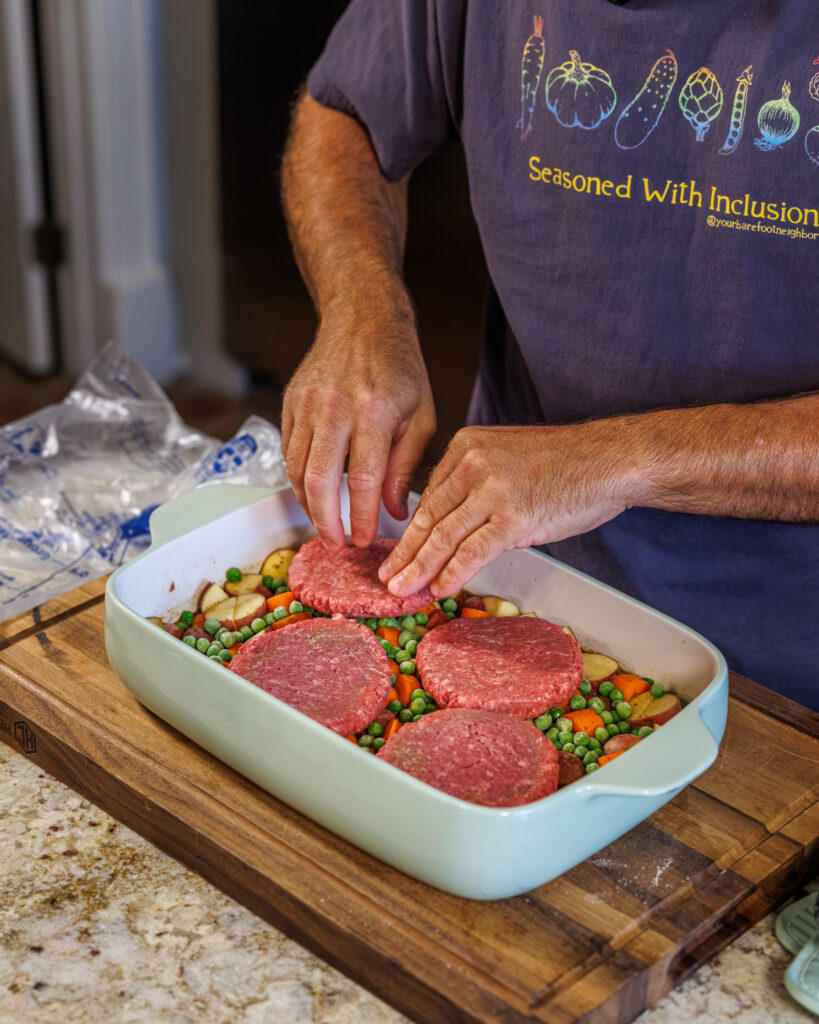 Matthew Bounds, creator of Your Barefoot Neighbor, places hamburger patties on top of chopped vegetables in a 9x13 dish for Hamburger Steaks and Gravy