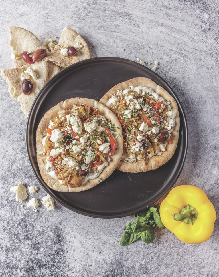 Your Barefoot Neighbor's Chicken Pita Wraps are piled high with chicken, feta cheese, and other ingredients sitting on a plate on the kitchen counter.