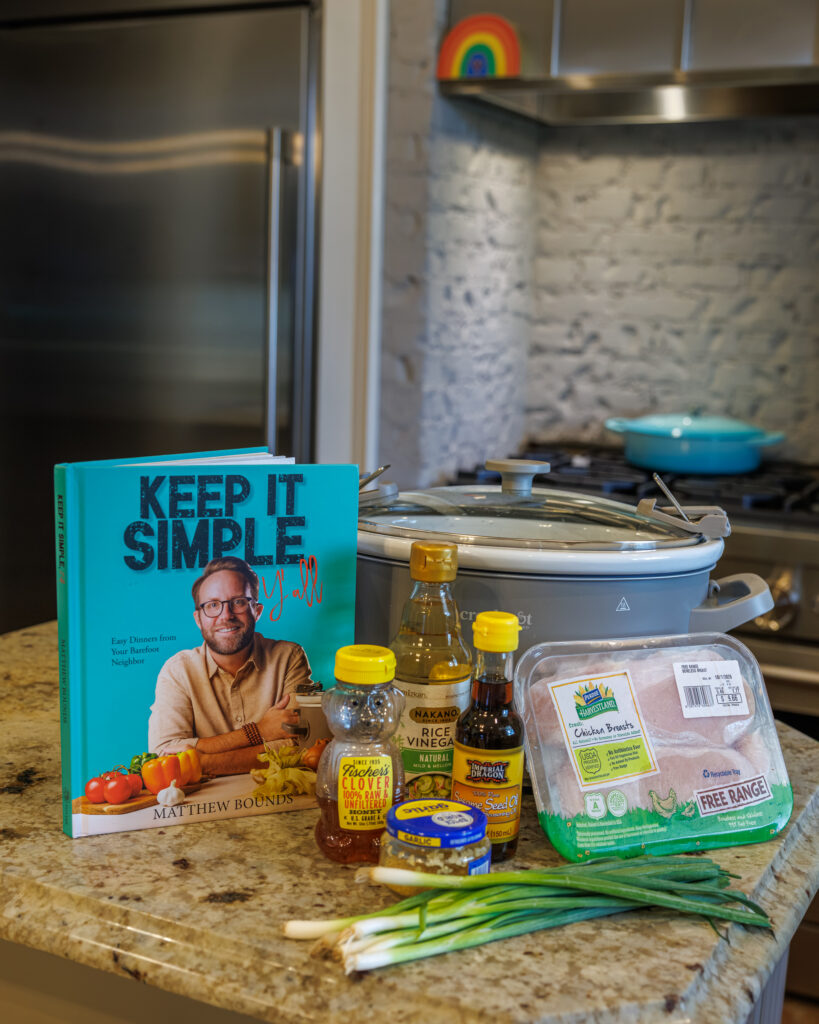 Your Barefoot Neighbor's Honey Garlic Chicken ingredients for the crockpot sit on the counter next to his book Keep It Simple Y'all
